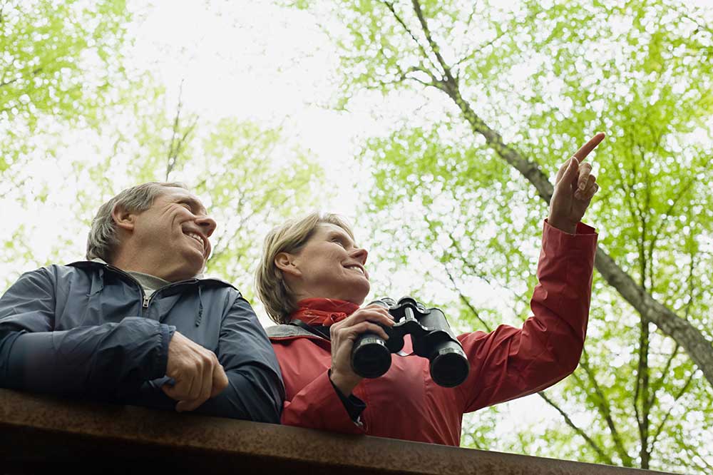 Middle aged couple in a wooded park with binoculars.
